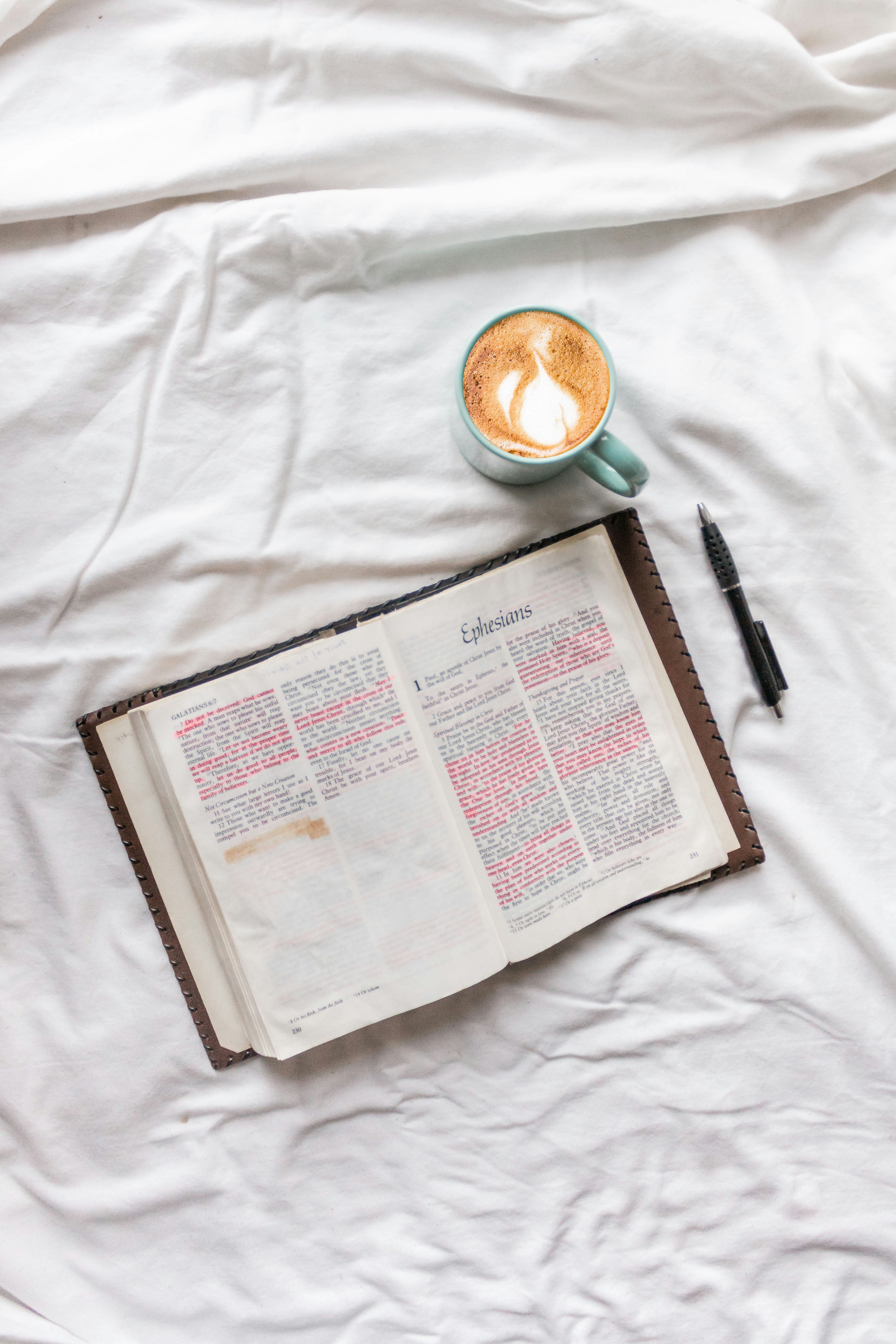 Open bible, cup of coffee, and pen on a white bedspread